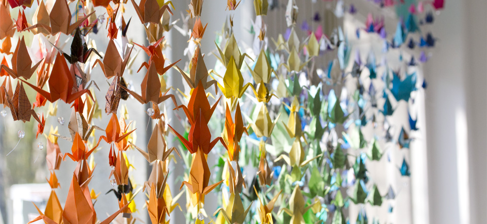 Schaufenstergestaltung in Regenbogenfarben: Origami Kraniche hängen im Kiezkaufhaus.