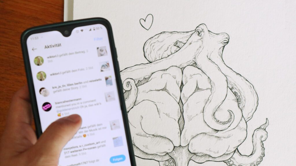 Das Smartphone zeigt die Aktivitäten in der App Instagram, im Hintergrund ein gezeichneter Oktopus mit einem Herzchen.
