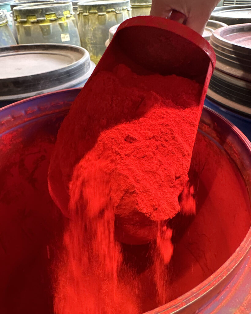 Rote Pigmente rieseln von einer großen Schaufel voll davon zurück in die Tonne.