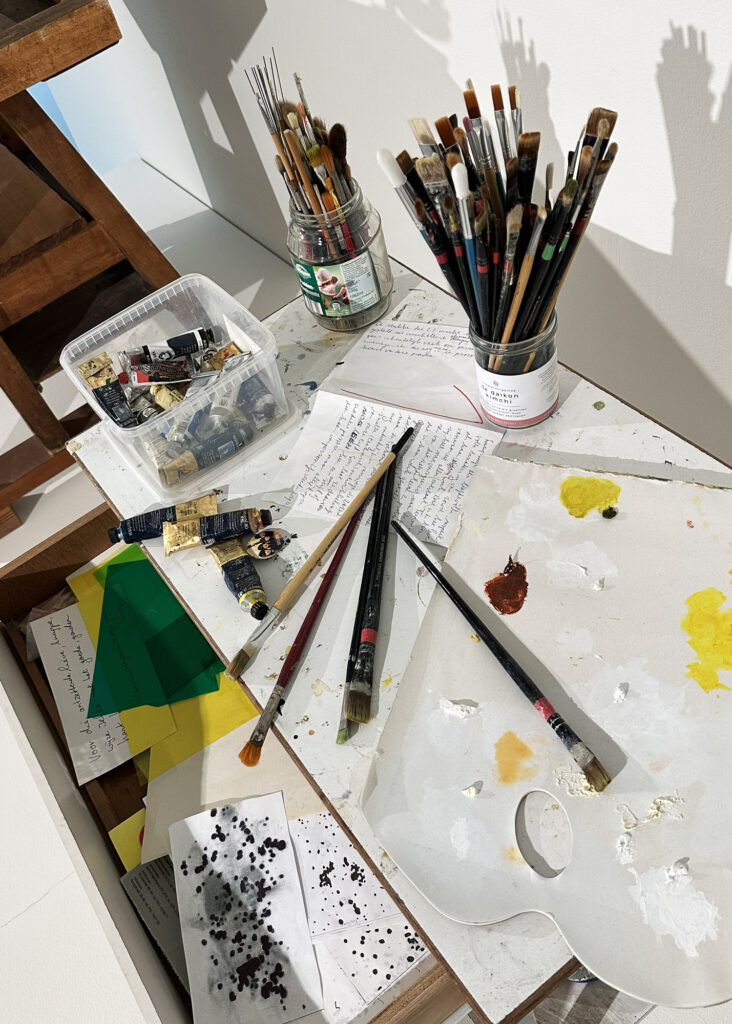 Ein Blick auf den Arbeitstisch von Jelle Kampen mit Pinseln, Farben und allerlei Notizen.