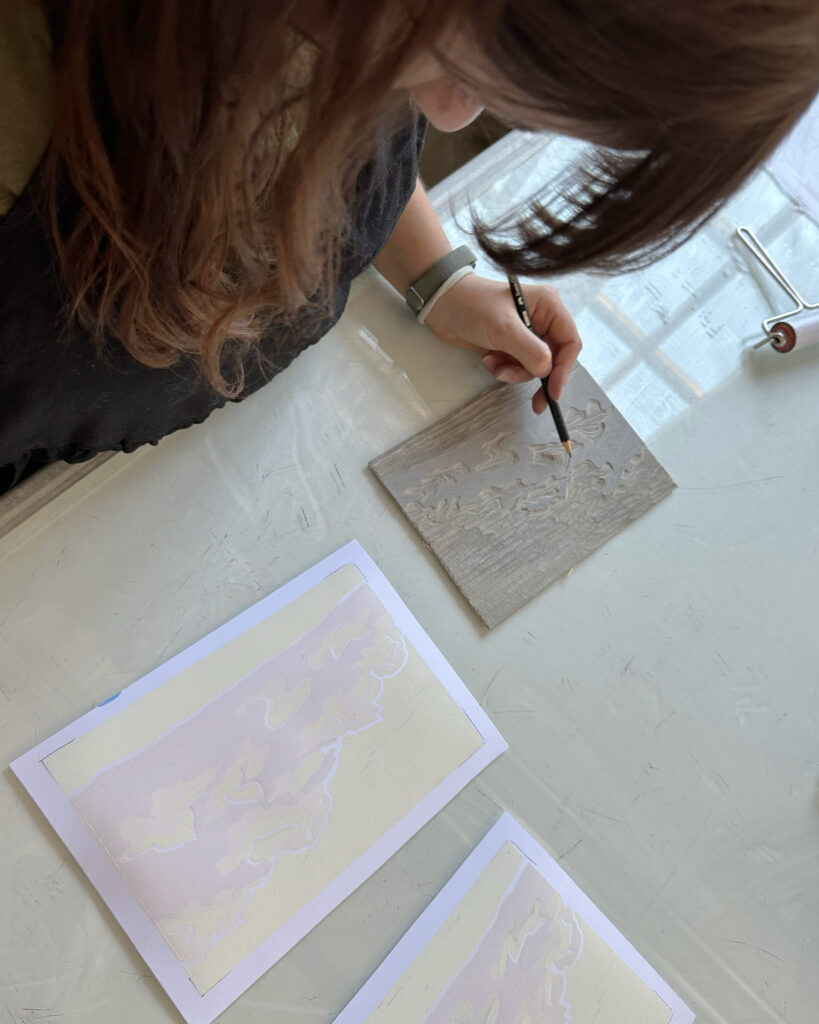 Anna plant die nächsten Schnitte in dem sie den Druck des Wolken-Motives genau betrachtet und mit Bleistift auf der Platte anzeichnet.