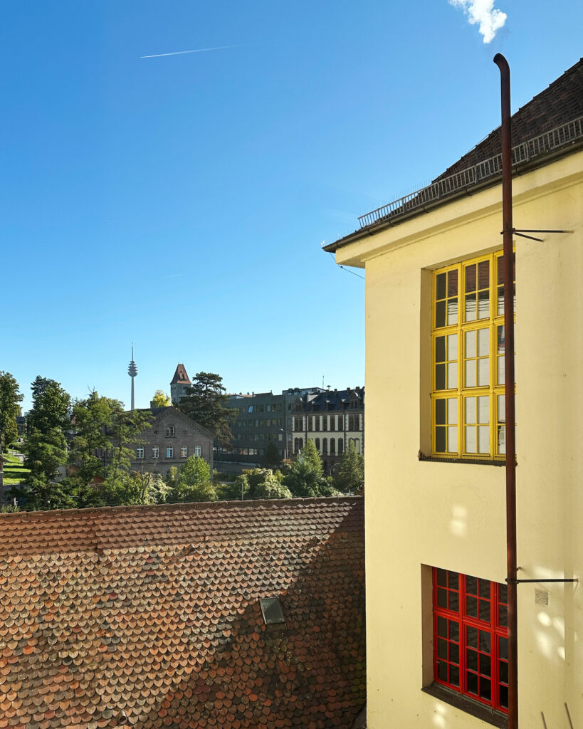 Blick aus einem Fenster der Akademie zum Firmengelände Faber-Castell mit dem Turm des Schlosses dahinter. Der Himmel ist strahlend blau.