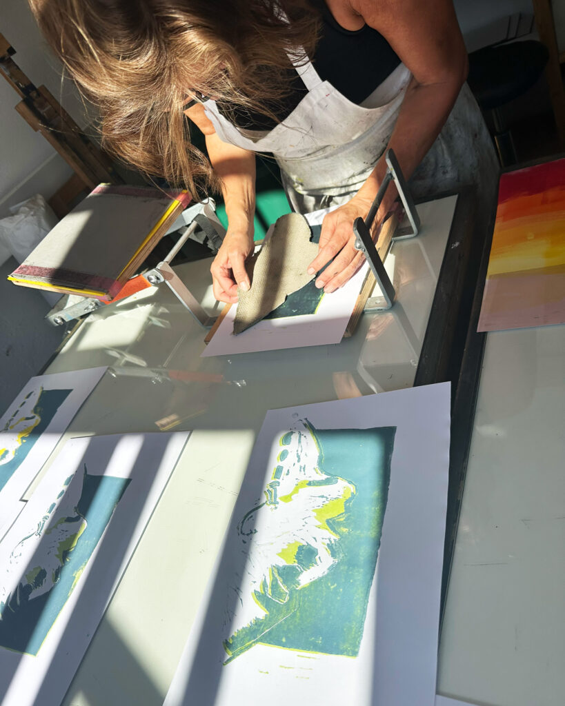 Bianca platziert die Druckplatte "frei Hand" auf dem Druck in der Hebelpresse. Davor liegt ein bereits gedrucktes Portrait.