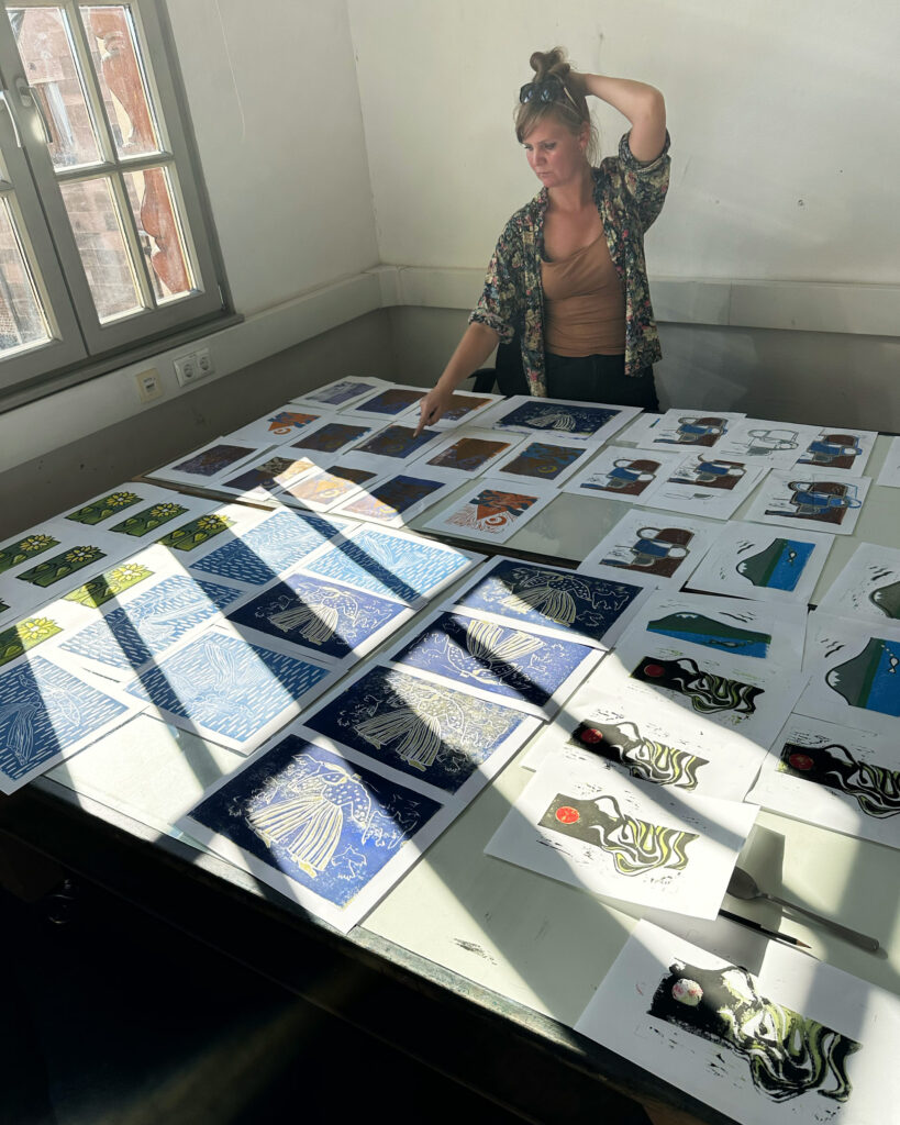 Caro begutachtet ihre und unsere Drucke vom ersten Tag, die zum Trocknen auf dem Tisch liegen.