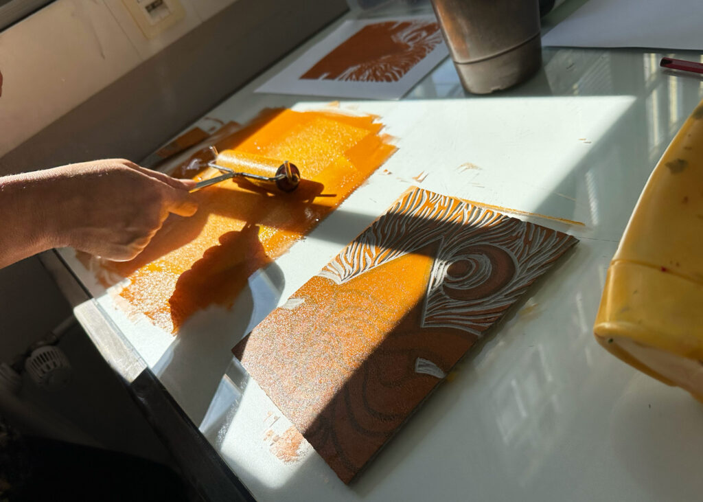 Caro färbt ihre Druckplatte mit der Walze in einem Orange-Ton ein.