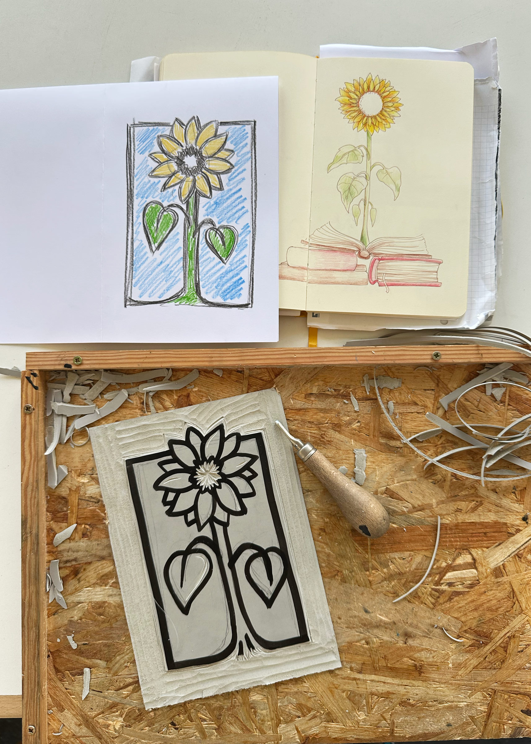 Aufgeschlagenes Skizzenbuch mit Vorlage, Farbskizze für den Druck und die Linolplatte mit den ersten weg genommen Flächen.