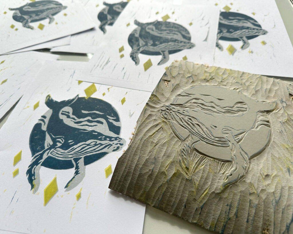 Die Drucke des Wal in den Wolken neben der Linoldruckplatte.