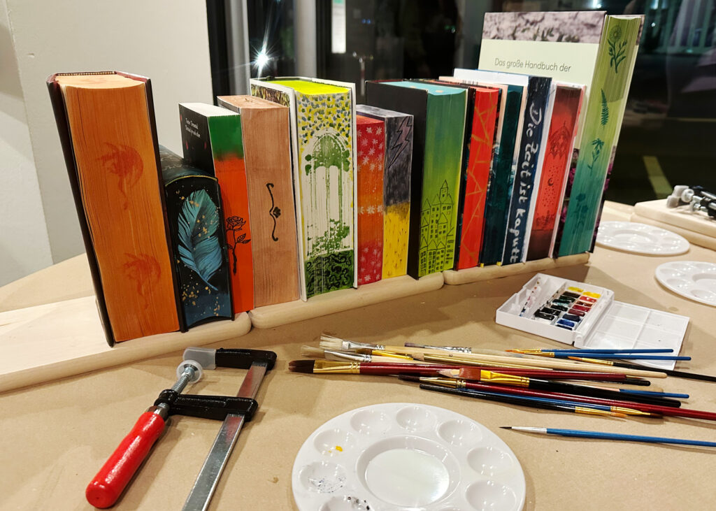 Die Ergebnisse des Workshops zusammen auf einem Bild: Die bemalten Bücher aufgereiht, so dass man die Seiten sieht.