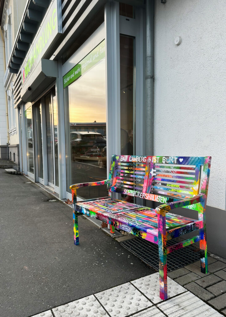 Vor dem Schaufenster der Buchhandlung Bücherbank steht eine bunt bemalte Bank.