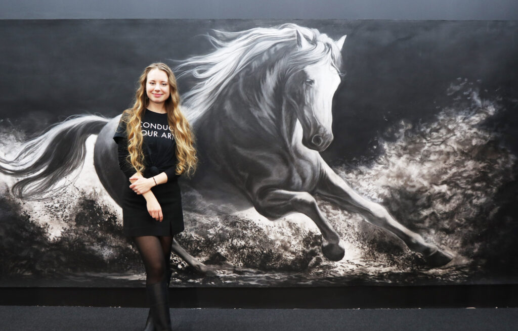 Künstlerin Zuzanna Salamon vor dem Wandfüllenden Kohle-Kunstwerk enstanden aus Nitram Fusain Aquarelle.